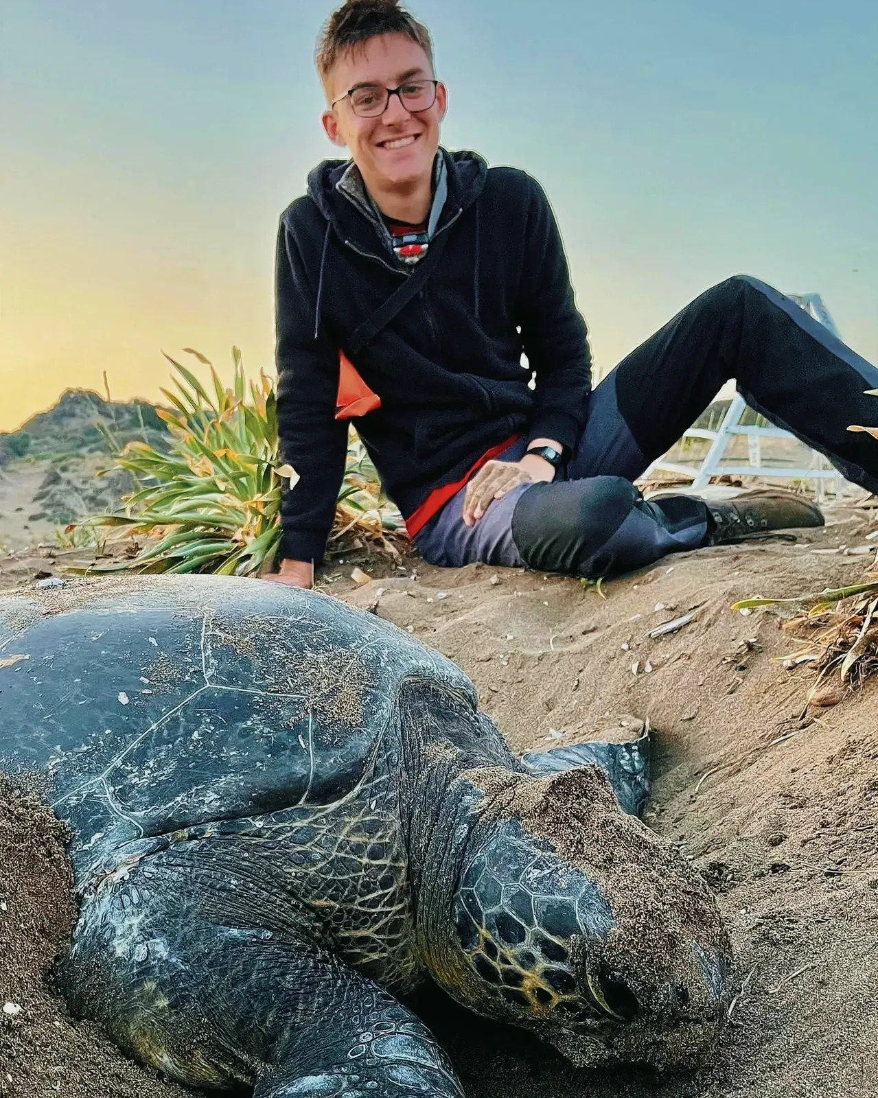 Man posing with a leatherback turtle on a sandy beach
