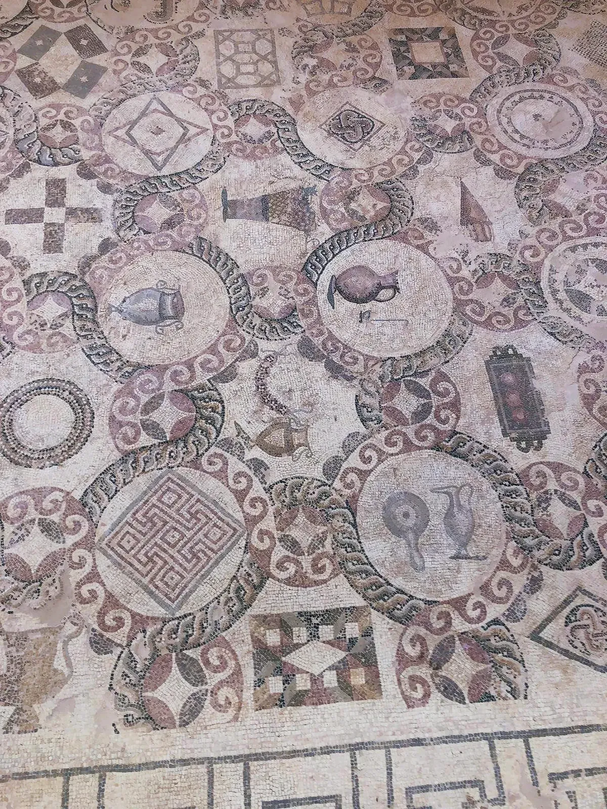 Intricate mosaic floor with cups, jug, sword, circle design, square with number, and bird