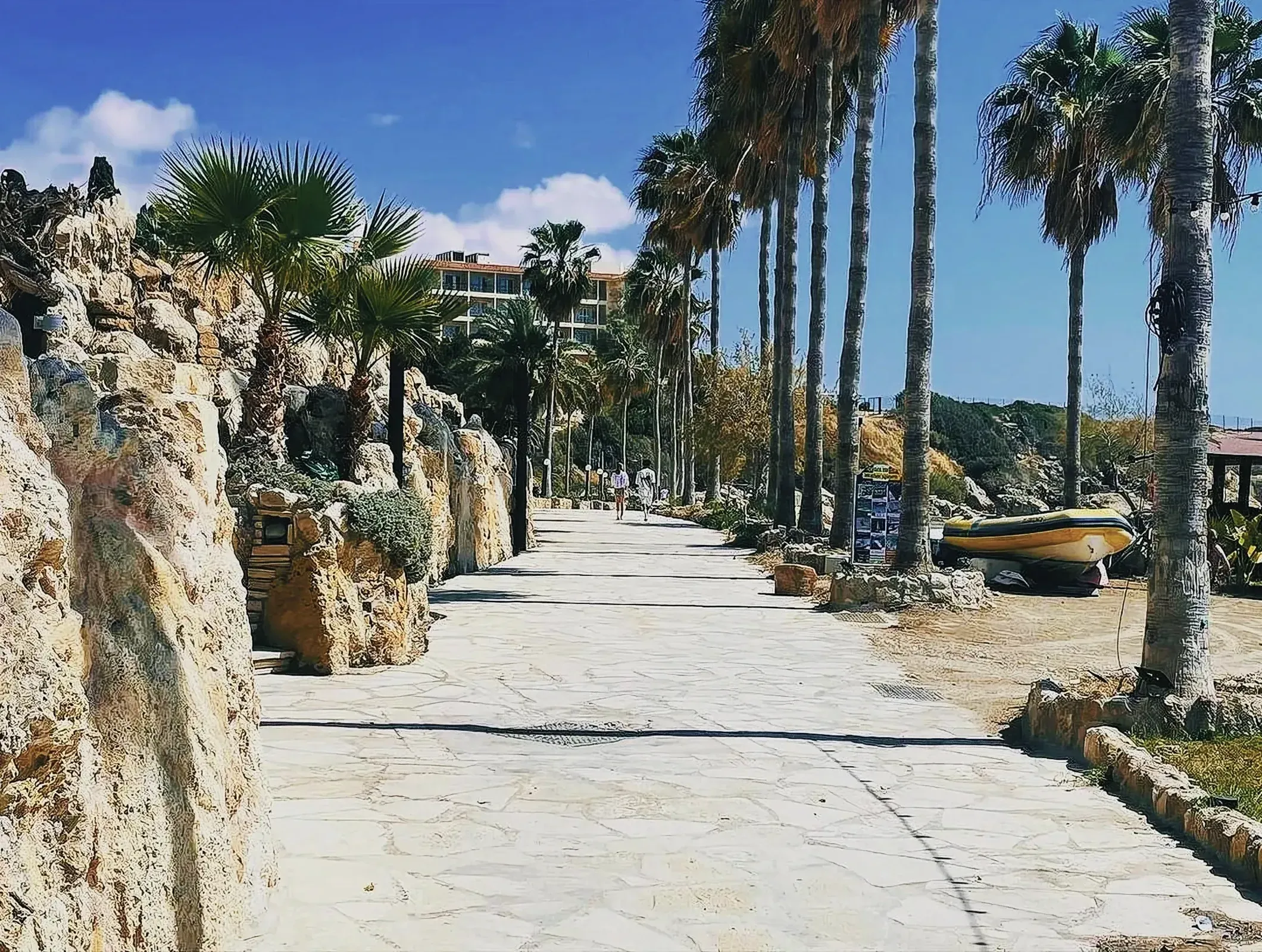 A picturesque view of Coral Bay in Cyprus with palm trees, a well-trodden path, and a boat resting on the side.