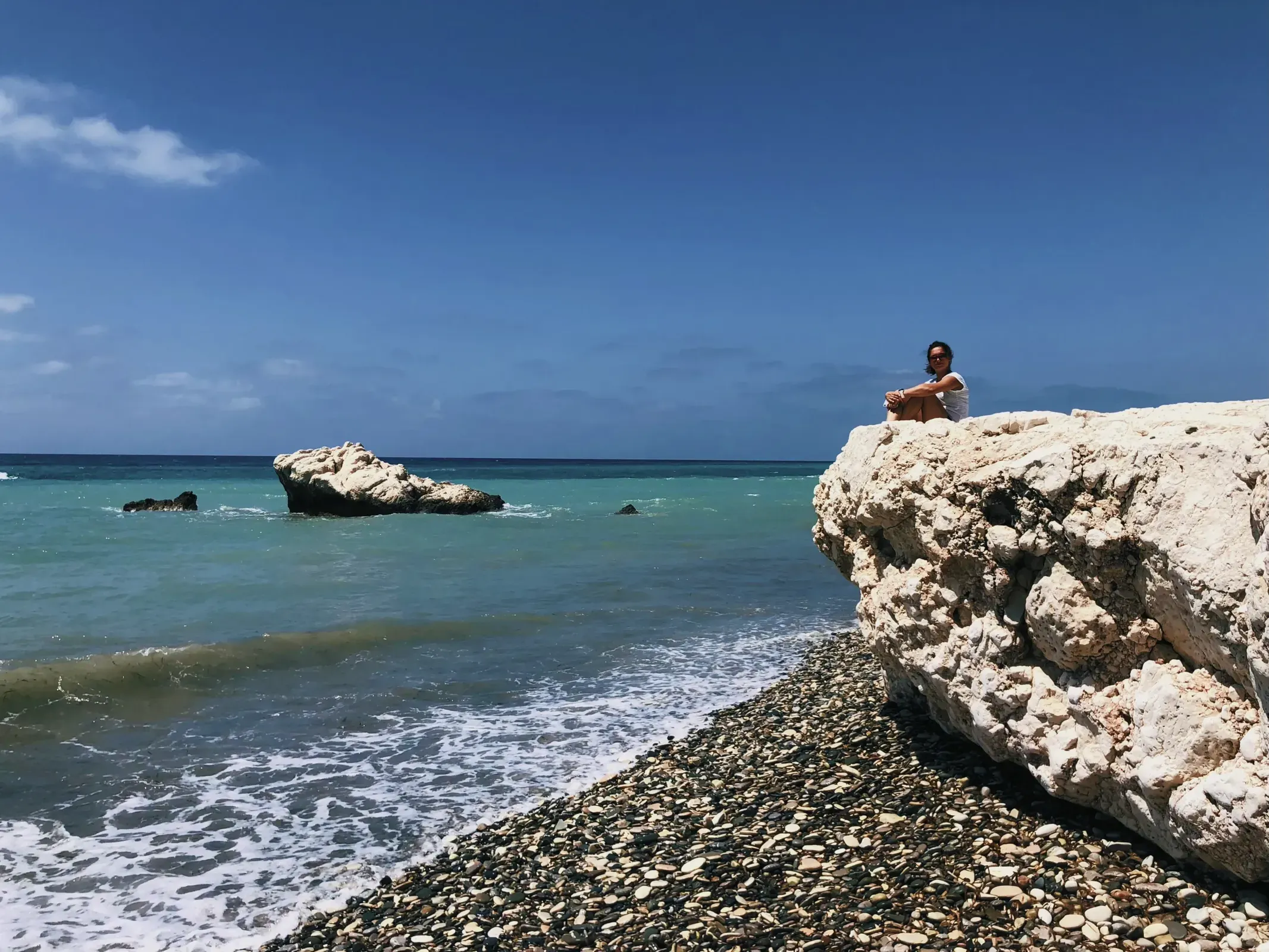 Serene scene at Aphrodite's Rock, a tropical beach with a single individual perched atop a rock.