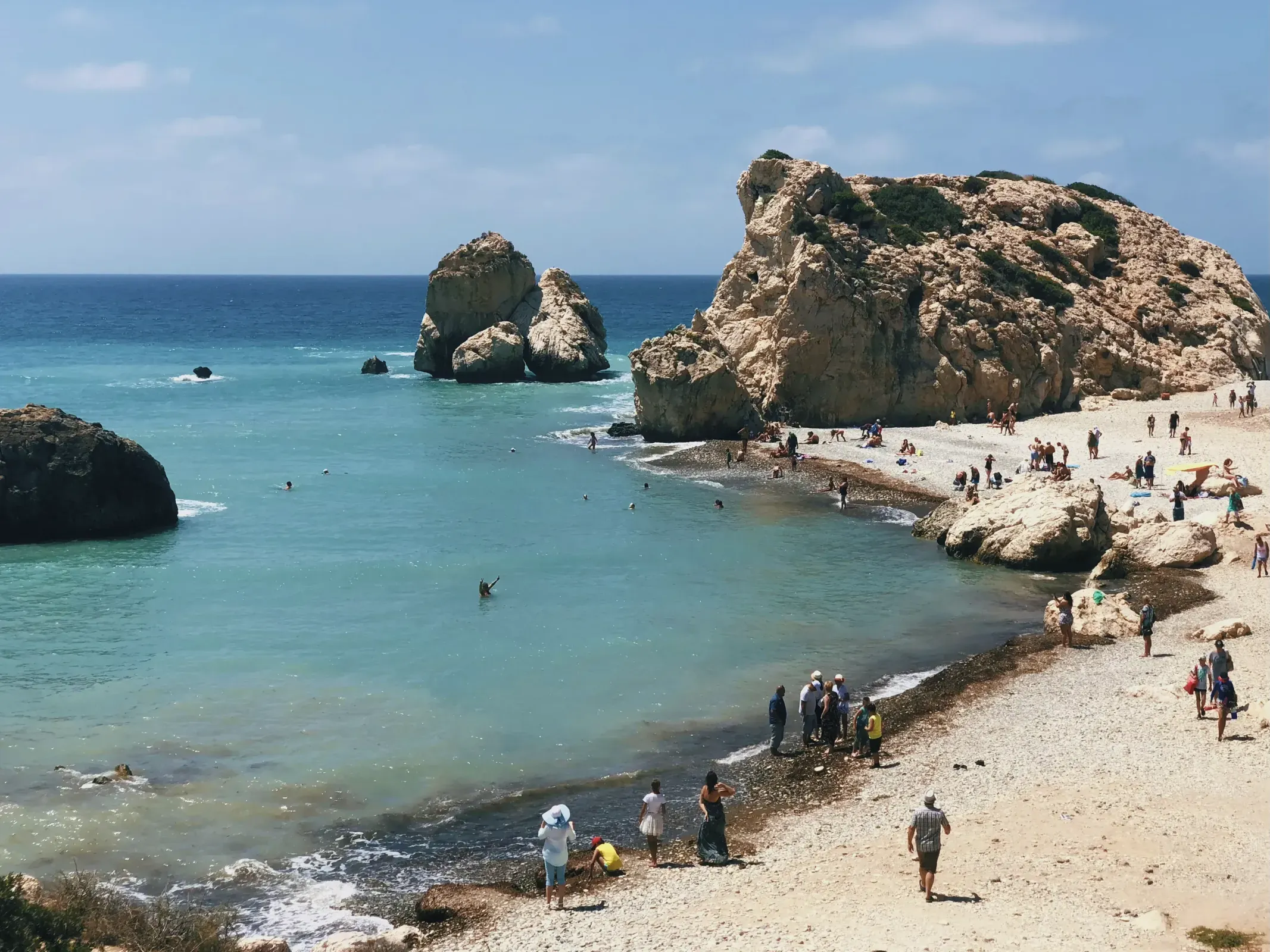 Group of people enjoying the beach with the iconic Petra tou Romiou rock formation in the background.